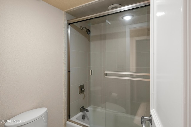 bathroom featuring toilet and shower / bath combination with glass door