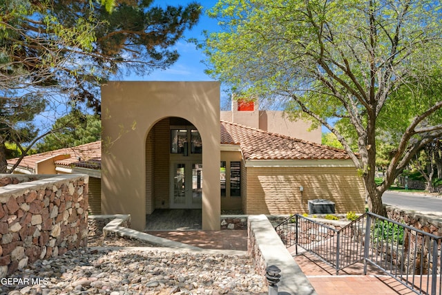 view of front facade featuring french doors, central AC, stucco siding, and a tile roof