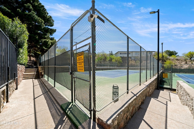 view of tennis court featuring fence and a gate