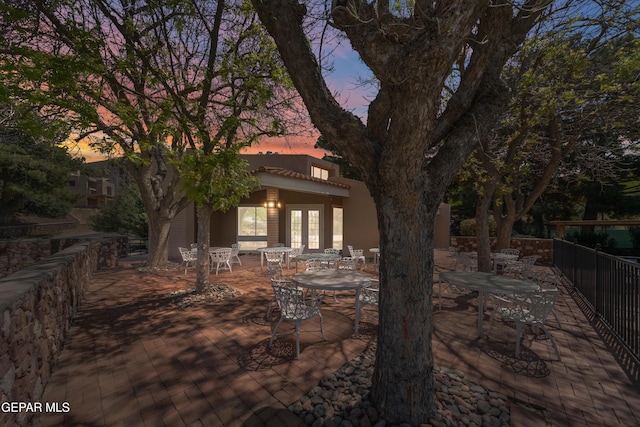 back of house at dusk featuring a patio, outdoor dining space, stucco siding, and fence
