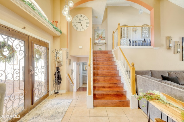 tiled entryway with stairway, arched walkways, french doors, and a high ceiling