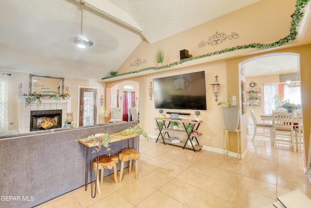 tiled living room featuring a tile fireplace, vaulted ceiling, a textured ceiling, and baseboards