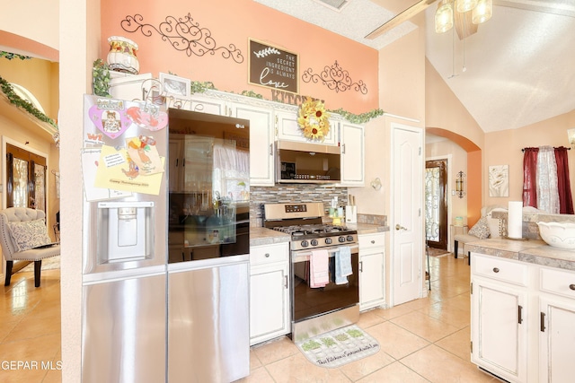 kitchen with decorative backsplash, light tile patterned floors, arched walkways, stainless steel appliances, and white cabinetry