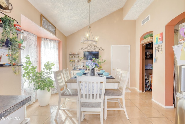 dining room with visible vents, light tile patterned floors, a chandelier, a textured ceiling, and high vaulted ceiling