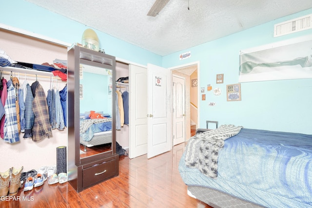 bedroom with a textured ceiling, wood finished floors, visible vents, and ceiling fan