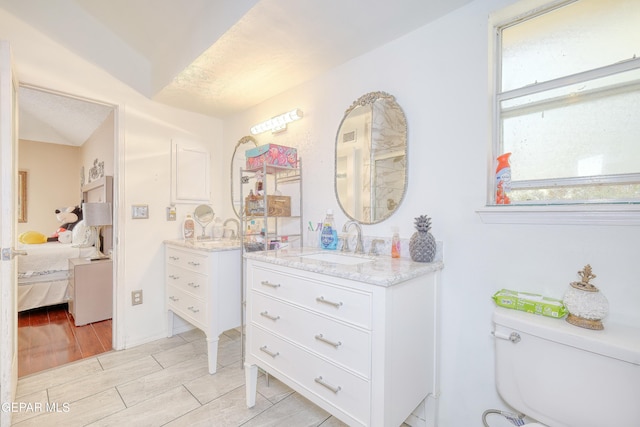 bathroom with two vanities, a sink, toilet, ensuite bath, and wood finish floors