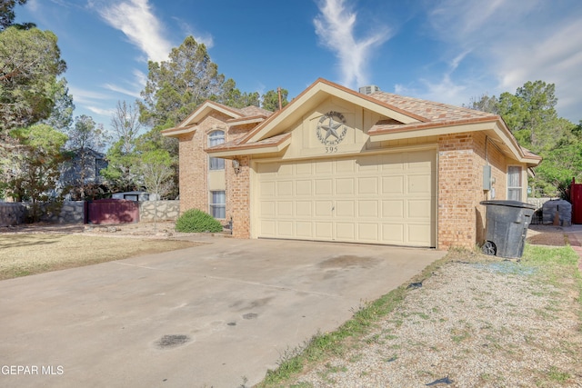 view of front of home featuring an attached garage, driveway, brick siding, and fence