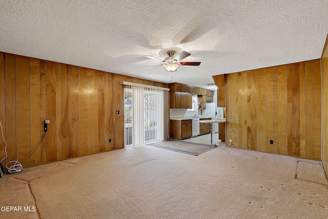 unfurnished living room with light colored carpet, wood walls, a ceiling fan, and a textured ceiling