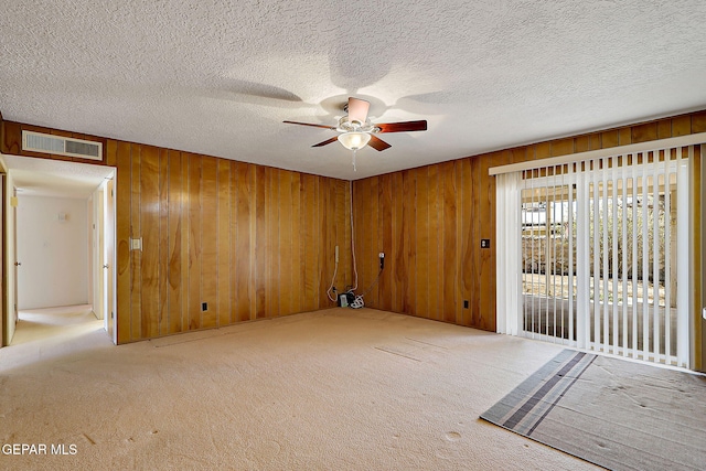 spare room with a textured ceiling, a ceiling fan, visible vents, carpet flooring, and wooden walls