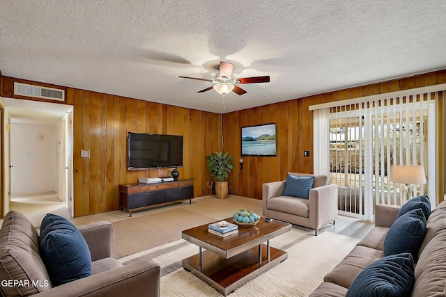 living room featuring light carpet, visible vents, a textured ceiling, and ceiling fan