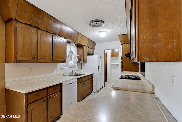 kitchen with a sink, white appliances, a textured ceiling, brown cabinetry, and light tile patterned flooring
