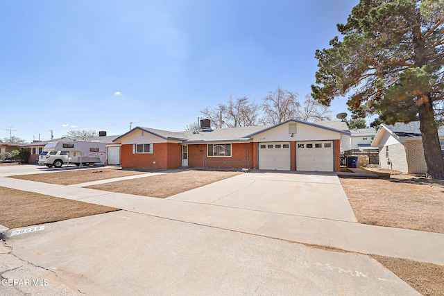 single story home with a garage, central air condition unit, driveway, and brick siding