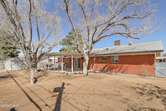rear view of house with an outdoor structure, a patio, fence, brick siding, and a chimney