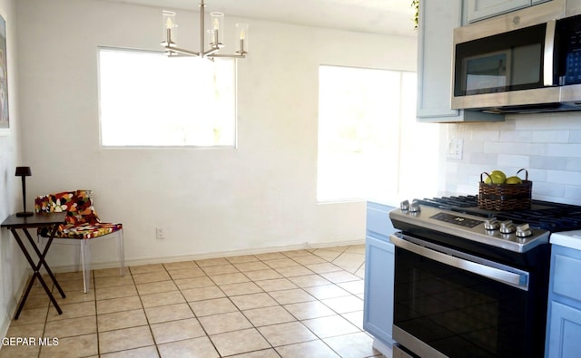 kitchen featuring baseboards, a notable chandelier, appliances with stainless steel finishes, decorative backsplash, and light tile patterned flooring