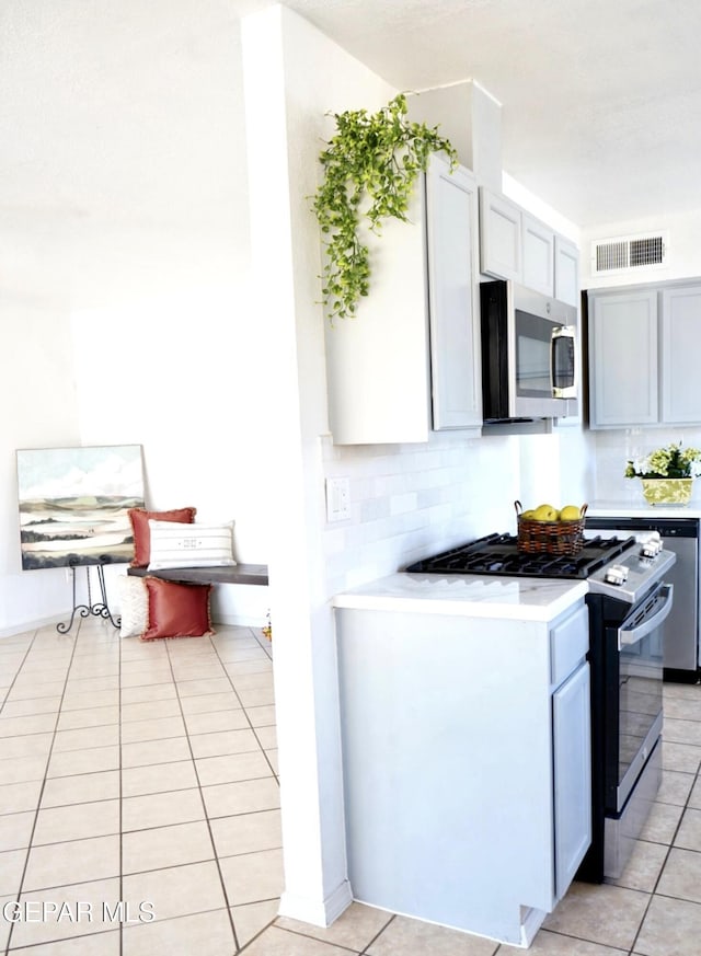 kitchen with stainless steel microwave, gas stove, light tile patterned floors, light countertops, and decorative backsplash