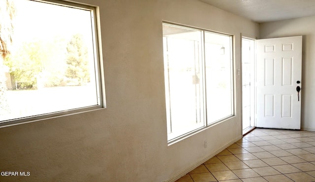 doorway with light tile patterned floors, baseboards, and a healthy amount of sunlight