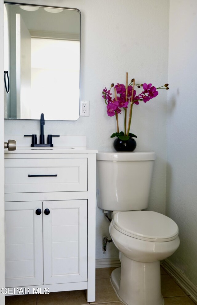 half bathroom with toilet, vanity, baseboards, and tile patterned flooring