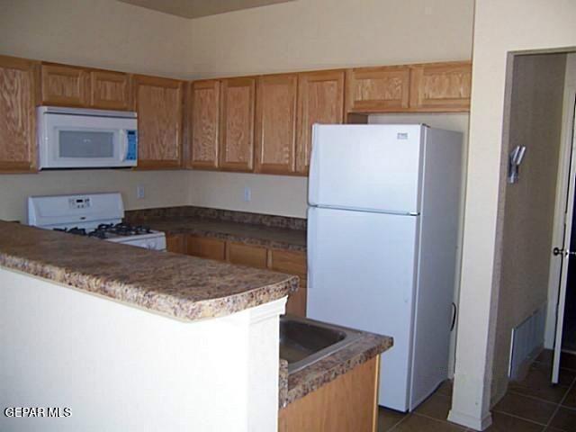 kitchen with a peninsula, white appliances, and dark tile patterned floors