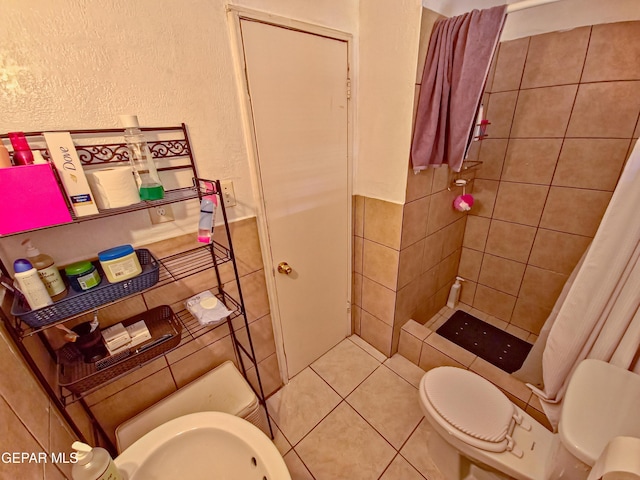 7726 Monterrey Dr, El Paso, TX 79915 - bathroom featuring toilet, tile walls, a tile shower, a wainscoted wall, and tile patterned flooring