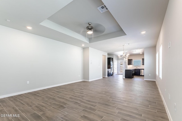 unfurnished living room with a tray ceiling, visible vents, ceiling fan with notable chandelier, and baseboards