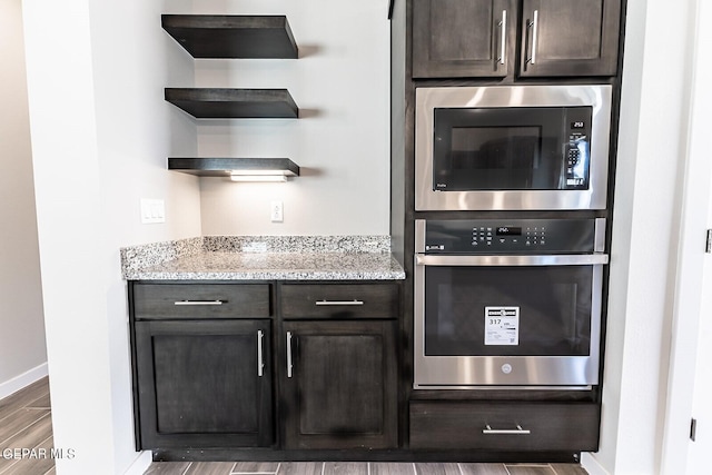 kitchen with light stone countertops, dark brown cabinets, wood finished floors, baseboards, and built in microwave