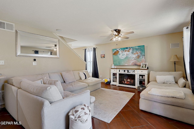 living area with a ceiling fan, dark wood-style flooring, and a glass covered fireplace