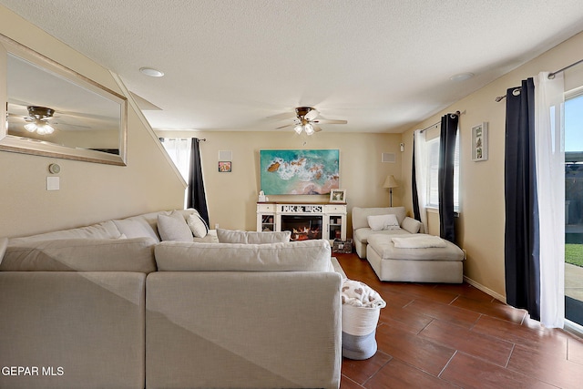 living room with ceiling fan, a glass covered fireplace, a textured ceiling, and baseboards