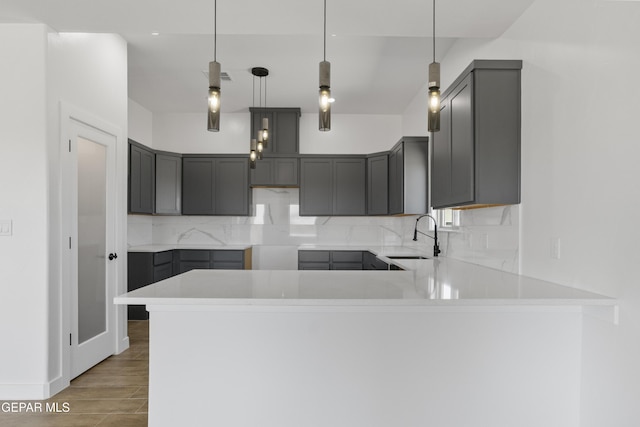 kitchen featuring a sink, a peninsula, wood finished floors, decorative backsplash, and gray cabinetry