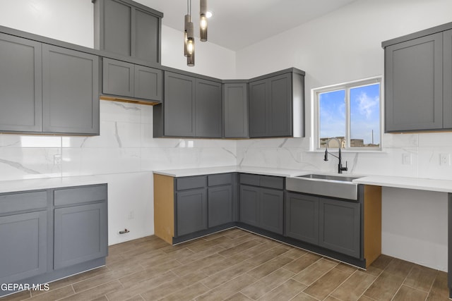 kitchen featuring decorative backsplash, wood finished floors, a sink, and gray cabinets