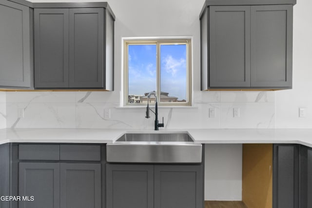 kitchen with backsplash, light countertops, gray cabinets, and a sink