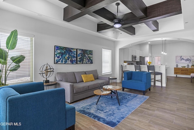 living area with baseboards, a ceiling fan, beamed ceiling, coffered ceiling, and arched walkways
