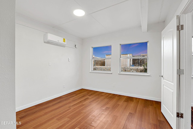spare room featuring light wood-type flooring, a wall mounted air conditioner, and baseboards