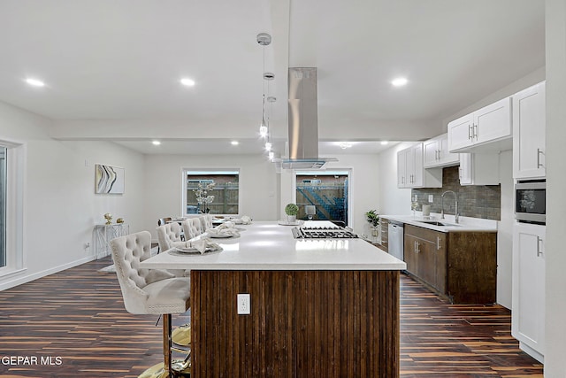 kitchen featuring dark wood finished floors, appliances with stainless steel finishes, island exhaust hood, light countertops, and a sink