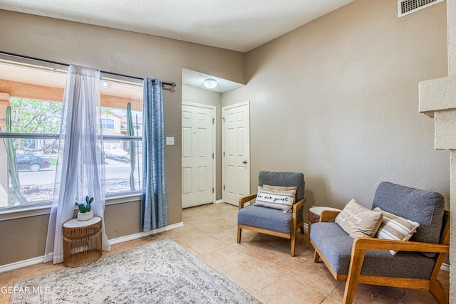 sitting room with visible vents, baseboards, light tile patterned flooring, and a textured wall