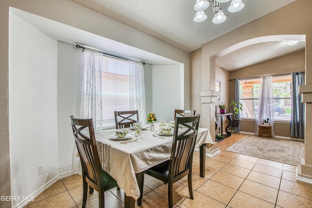 dining space featuring a notable chandelier, a textured wall, light tile patterned floors, a textured ceiling, and arched walkways