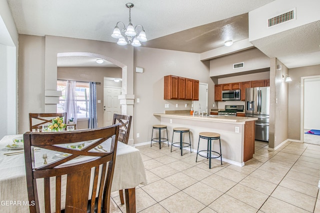 kitchen featuring visible vents, arched walkways, appliances with stainless steel finishes, a breakfast bar, and light tile patterned flooring