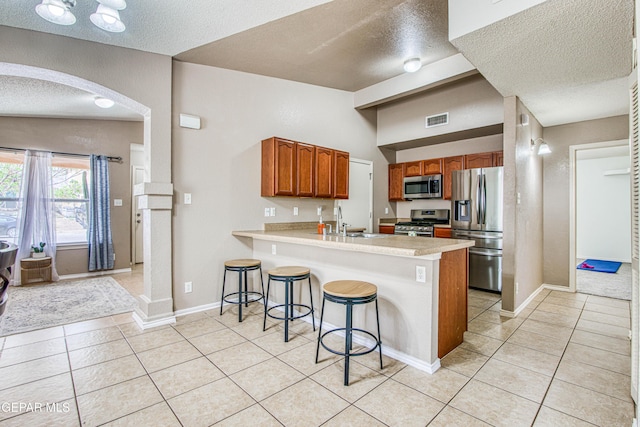 kitchen with light tile patterned floors, a peninsula, a textured ceiling, appliances with stainless steel finishes, and arched walkways
