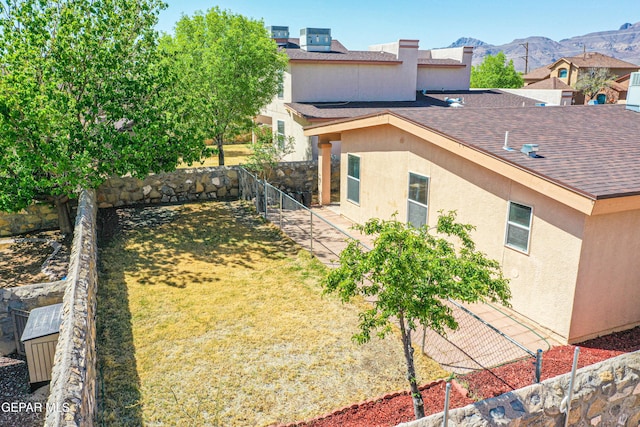 exterior space featuring a yard, a fenced backyard, stucco siding, a shingled roof, and a mountain view