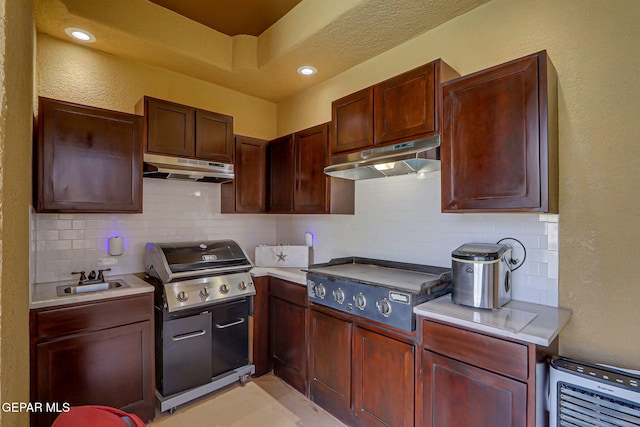 kitchen with under cabinet range hood, light countertops, a sink, and backsplash