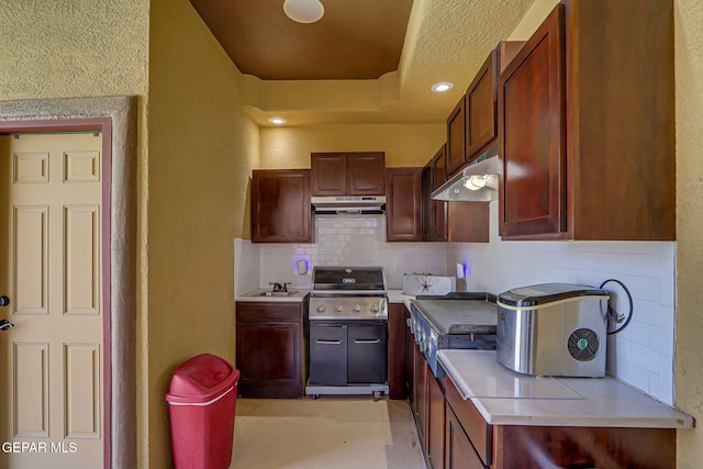 kitchen featuring light countertops, tasteful backsplash, under cabinet range hood, and a sink
