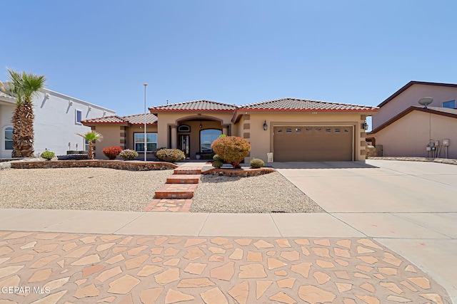 mediterranean / spanish house featuring a tiled roof, concrete driveway, a garage, and stucco siding