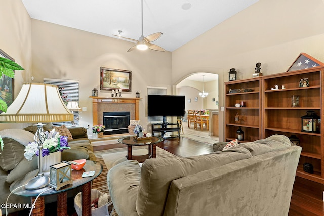 living room featuring vaulted ceiling, a tiled fireplace, dark wood-type flooring, arched walkways, and ceiling fan with notable chandelier
