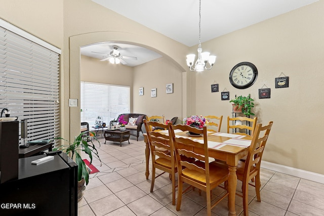 dining room featuring arched walkways, light tile patterned floors, ceiling fan with notable chandelier, and baseboards
