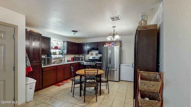 kitchen featuring light tile patterned floors, light countertops, under cabinet range hood, visible vents, and stainless steel appliances