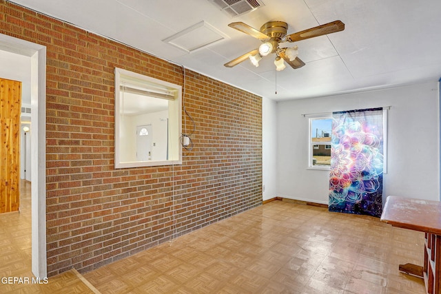 spare room featuring brick wall, ceiling fan, baseboards, and visible vents