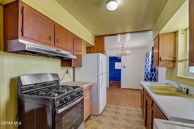 kitchen featuring black range with gas cooktop, under cabinet range hood, light countertops, a sink, and a notable chandelier
