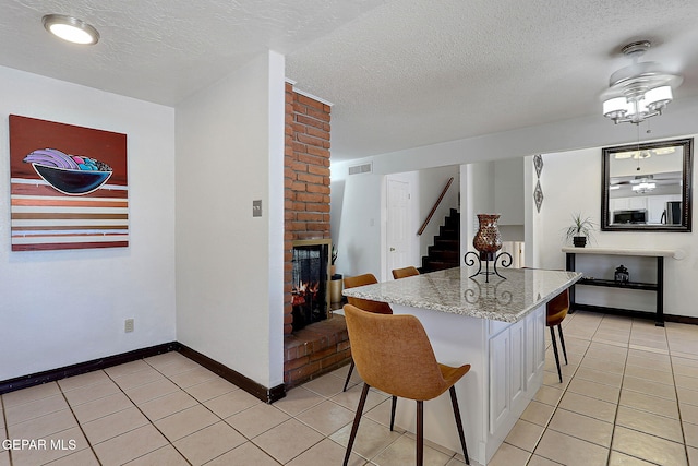 3705 Roslyn Dr, Horizon City, TX 79928 - kitchen featuring visible vents, a brick fireplace, a kitchen bar, light tile patterned floors, and baseboards