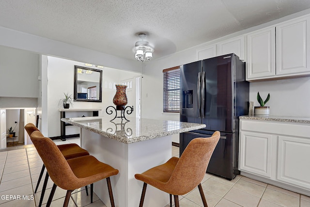 3705 Roslyn Dr, Horizon City, TX 79928 - kitchen featuring black fridge, light tile patterned flooring, white cabinetry, and a kitchen breakfast bar