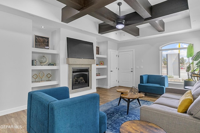 living area featuring ceiling fan, beamed ceiling, wood finished floors, coffered ceiling, and a glass covered fireplace