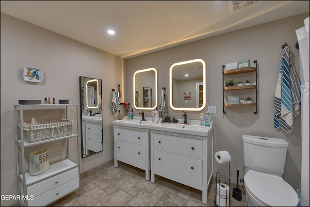 full bathroom with a sink, stone tile flooring, toilet, and two vanities